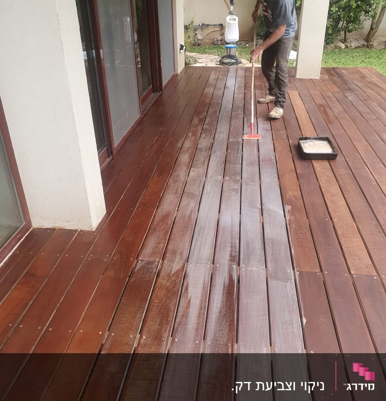 אדם מורח שמן על דק עץ בגינה